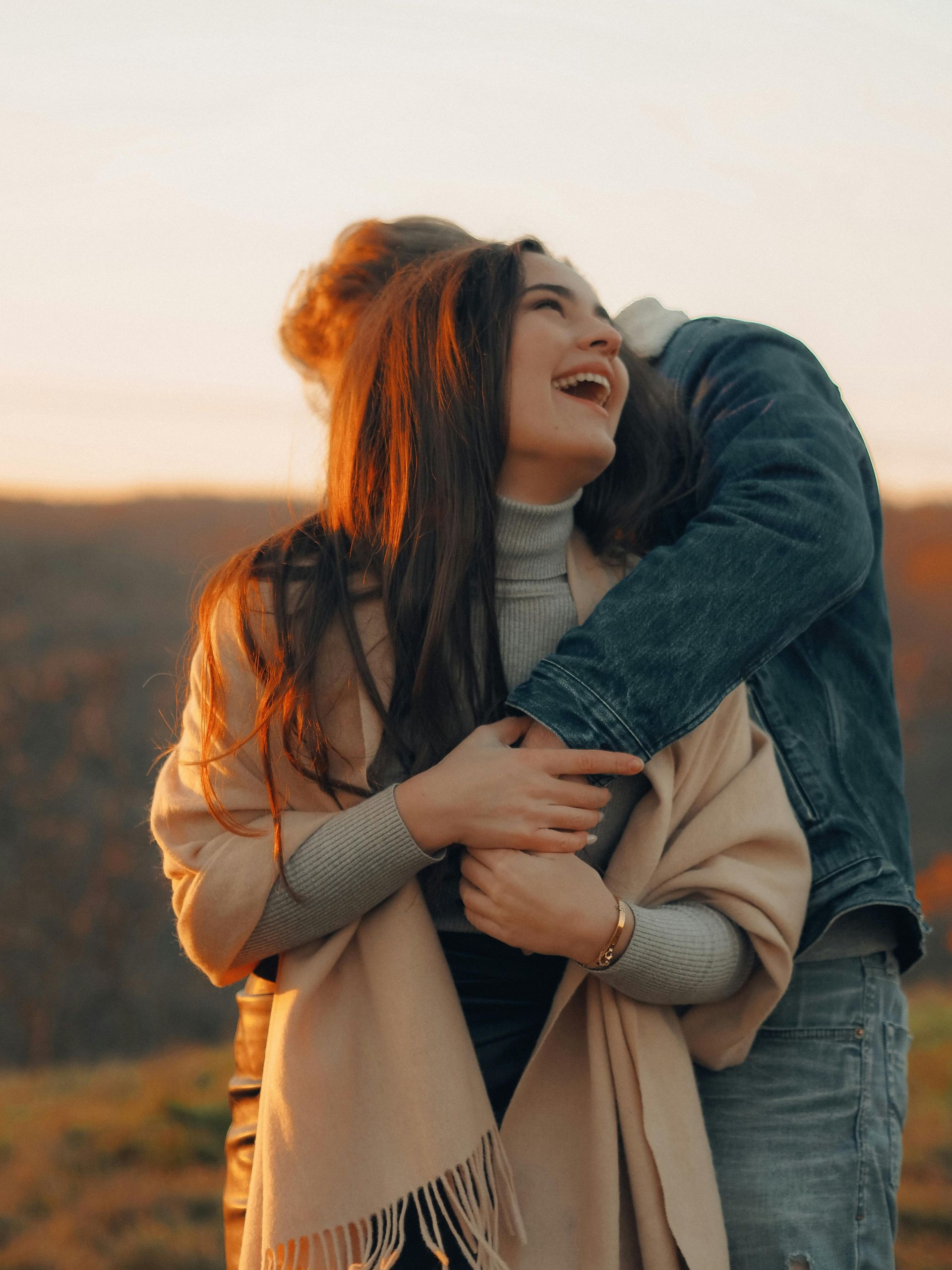 Two people hugging outdoors at sunset, smiling in warm golden light.