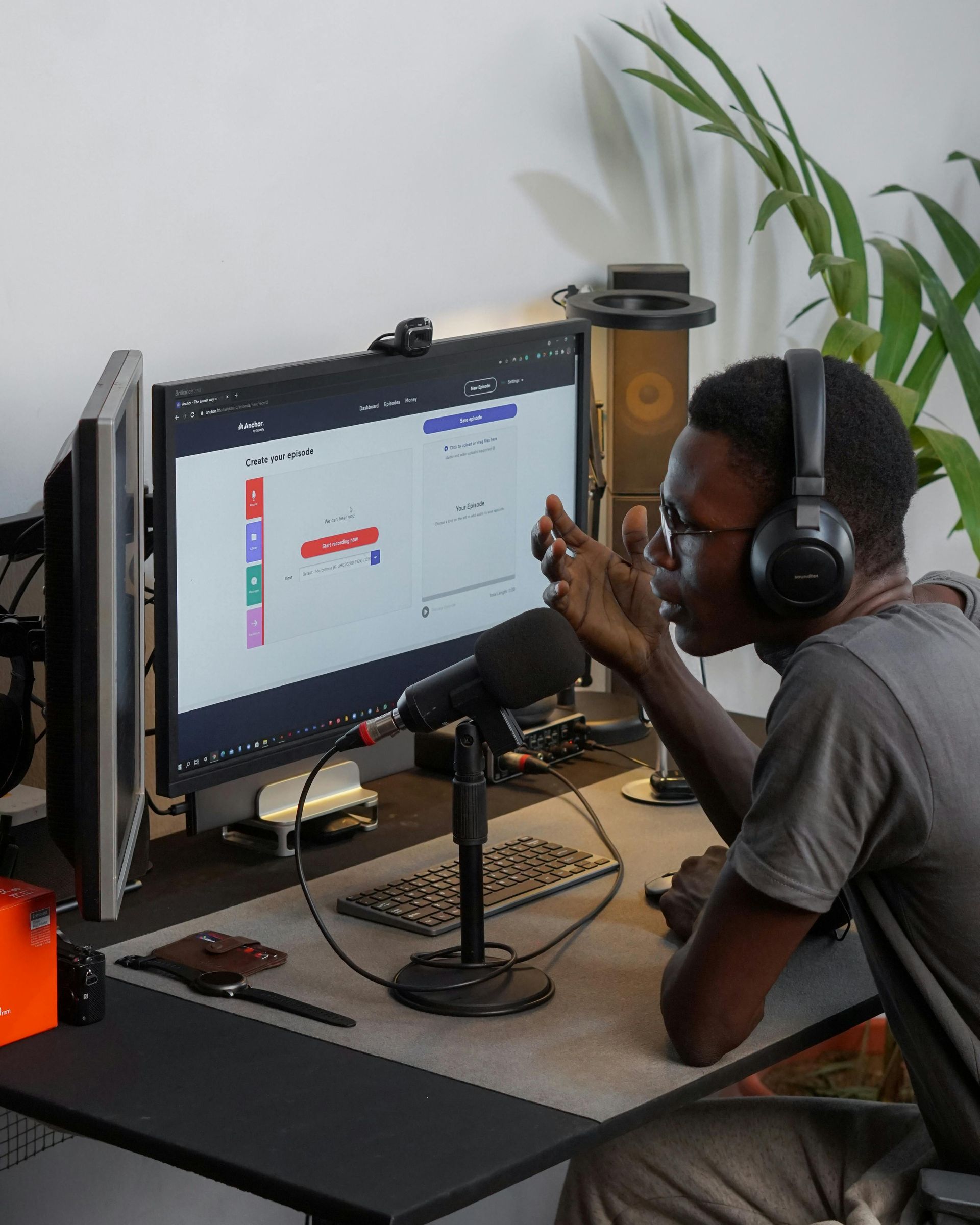Person wearing headphones works at a desk with a large monitor in a home office.