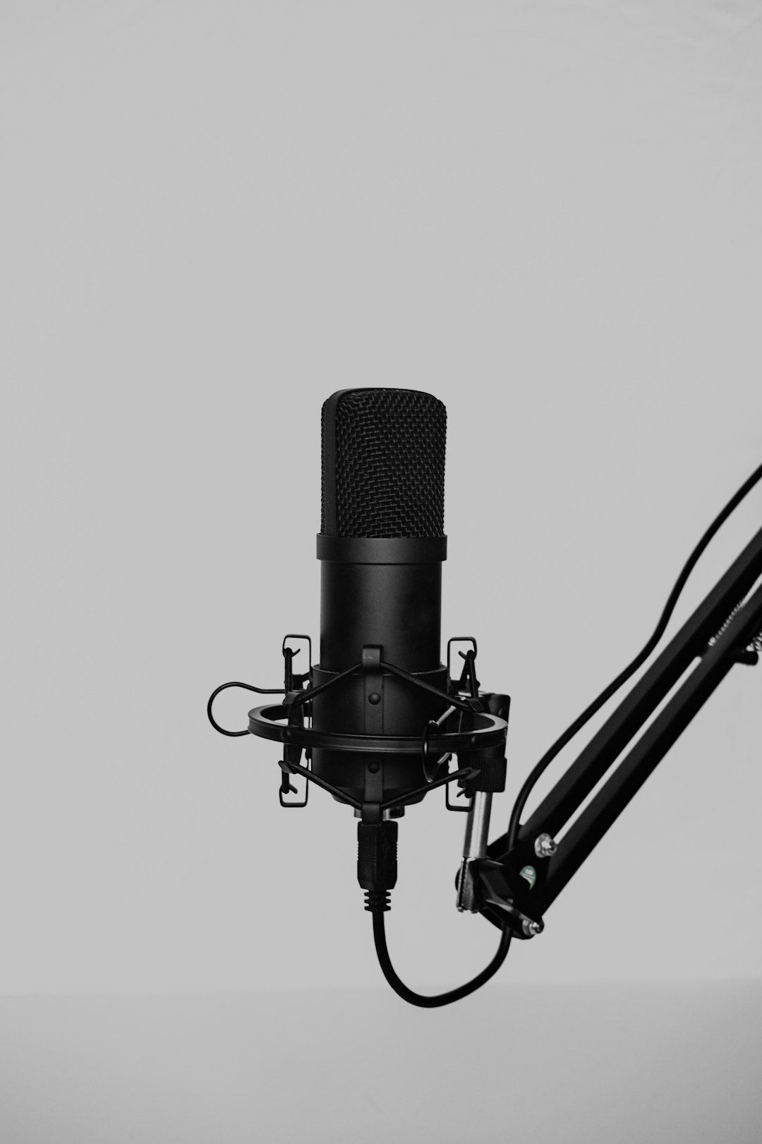 Black studio microphone on a boom arm against a plain light gray background.