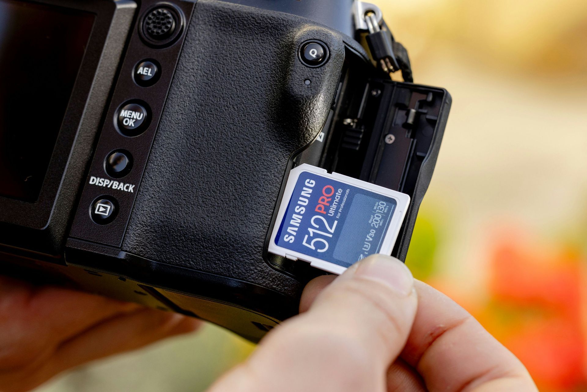 A hand inserts a 512MB SD card into a black digital camera.
