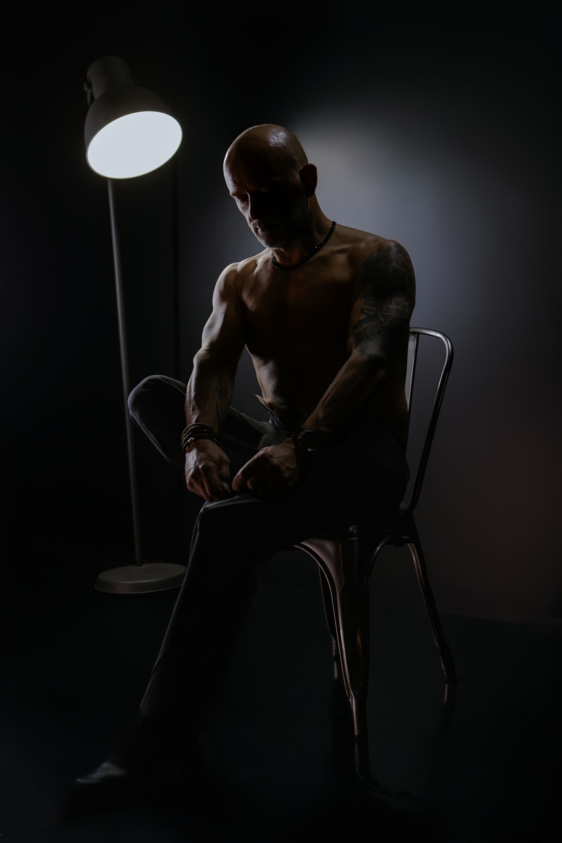 Dimly lit seated person in a chair beside a standing lamp, silhouetted against a dark background