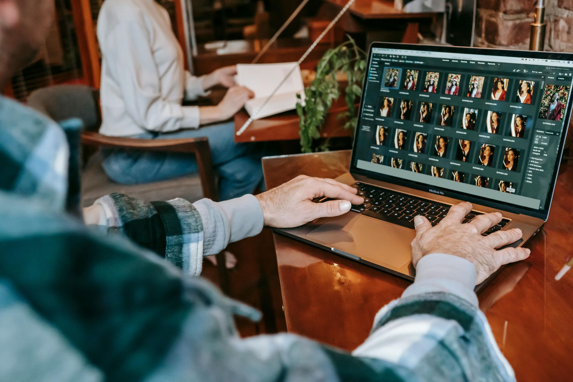 Person typing on a laptop beside a desktop monitor showing a video call in a café