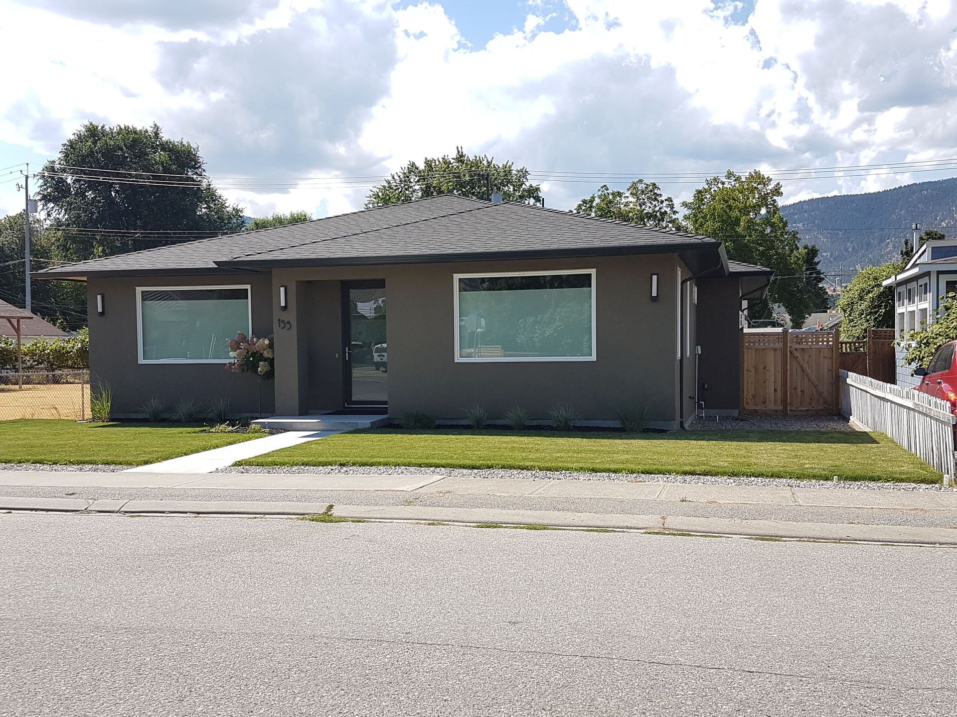 A modern low-rise house with a gray facade, large windows, central entrance, green lawn and concrete driveway.