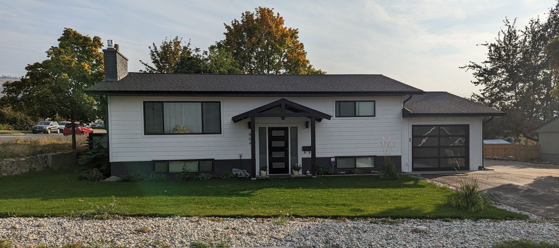 Two-story house with white siding and black base, central entry porch, garage, gray roof, and landscaped yard with trees.