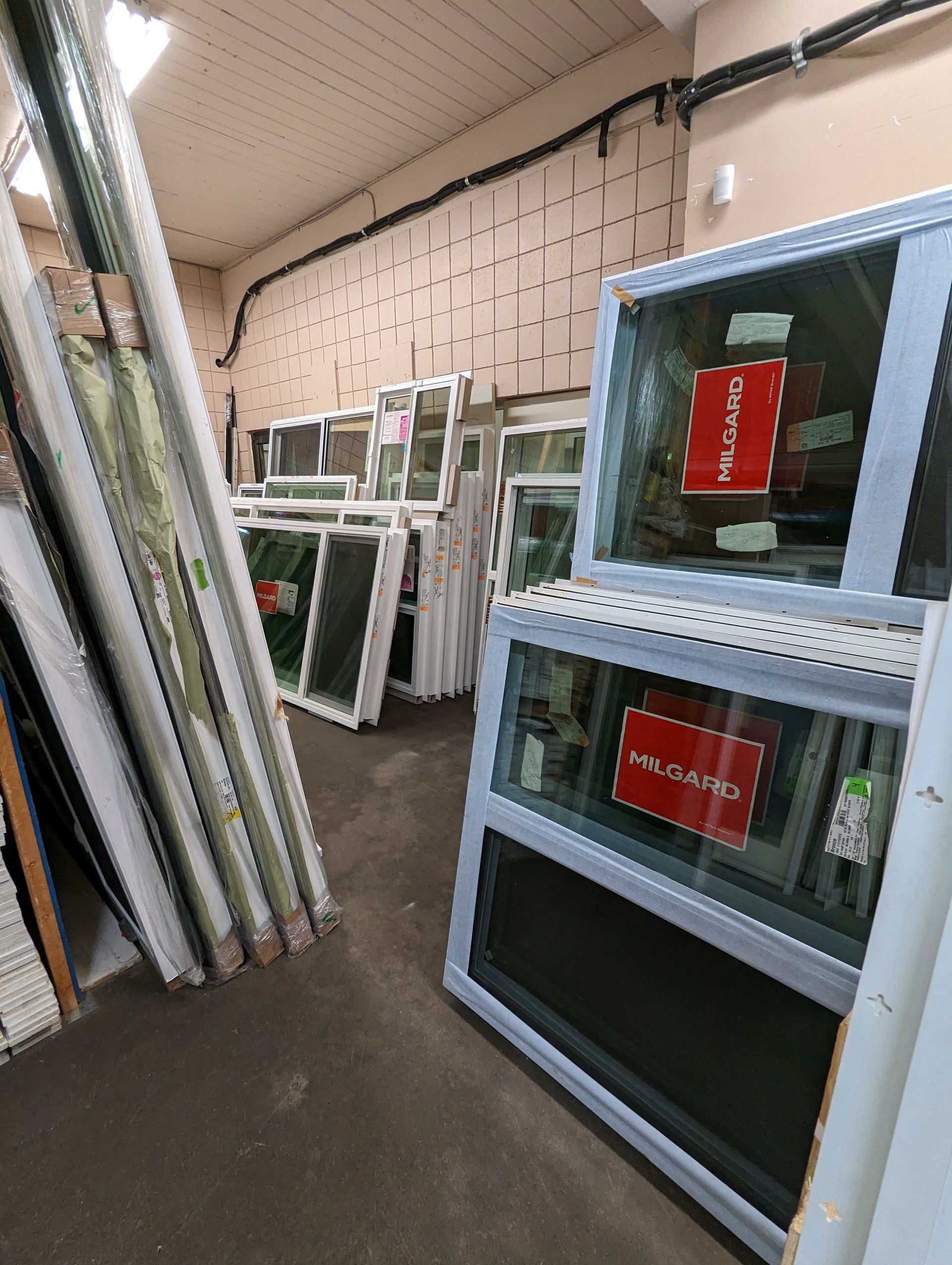 Warehouse showing white windows and doors stacked on the left, window display units on the right with information panels.