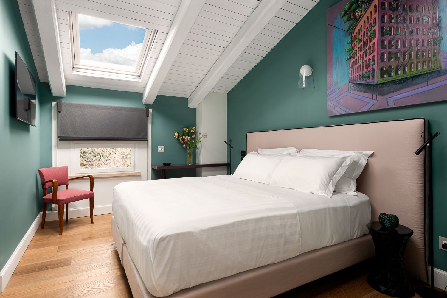 Bedroom with bed, skylight, wooden floor, teal walls, artwork, and chair.