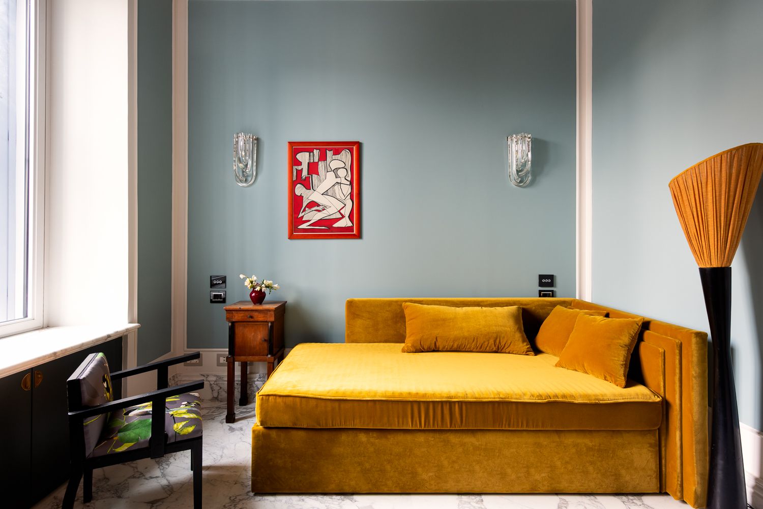 Mustard yellow sofa against a teal wall with a red-framed artwork and a patterned marble floor.