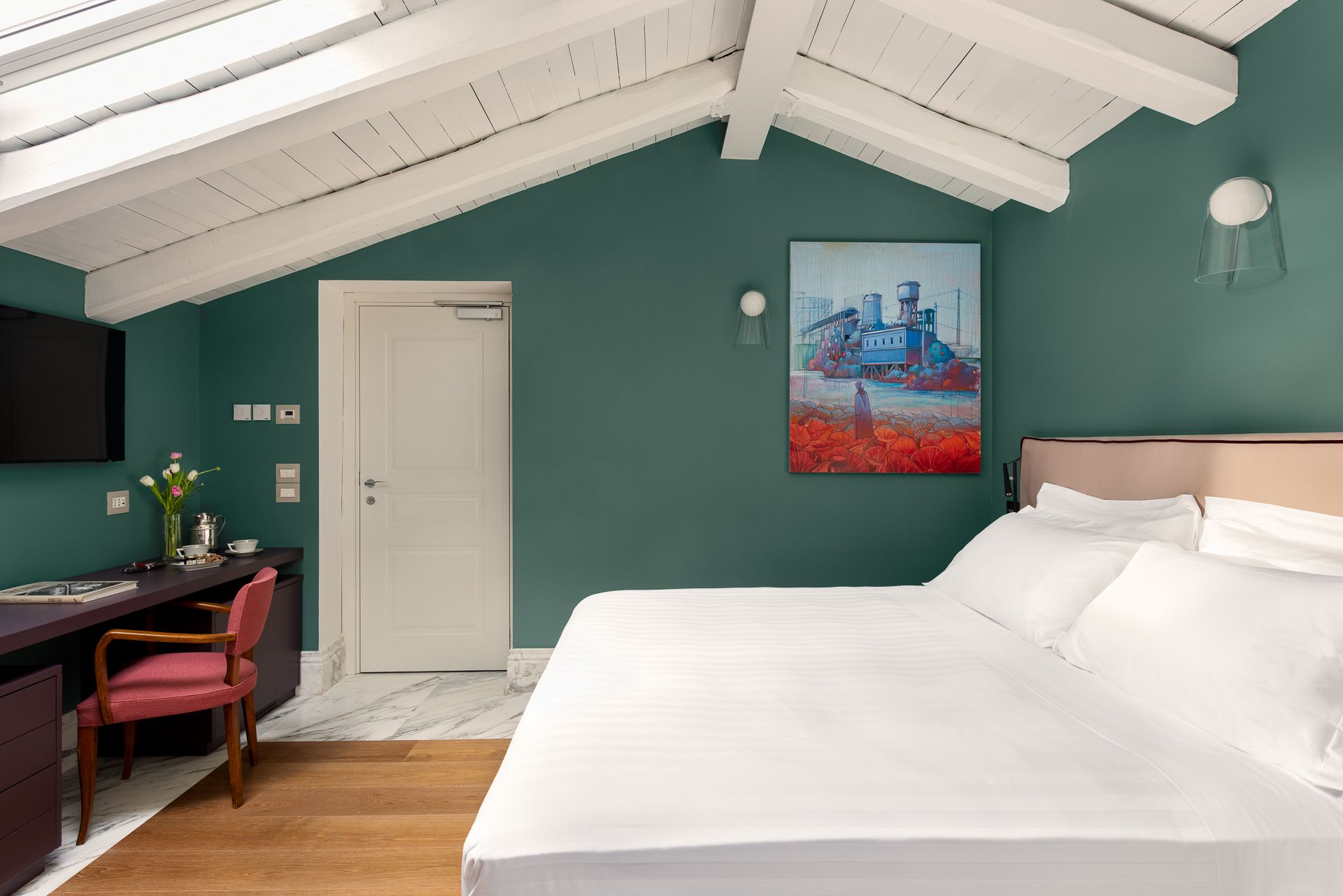 Bedroom with angled ceiling, green wall, double bed, desk, artwork, and white door.
