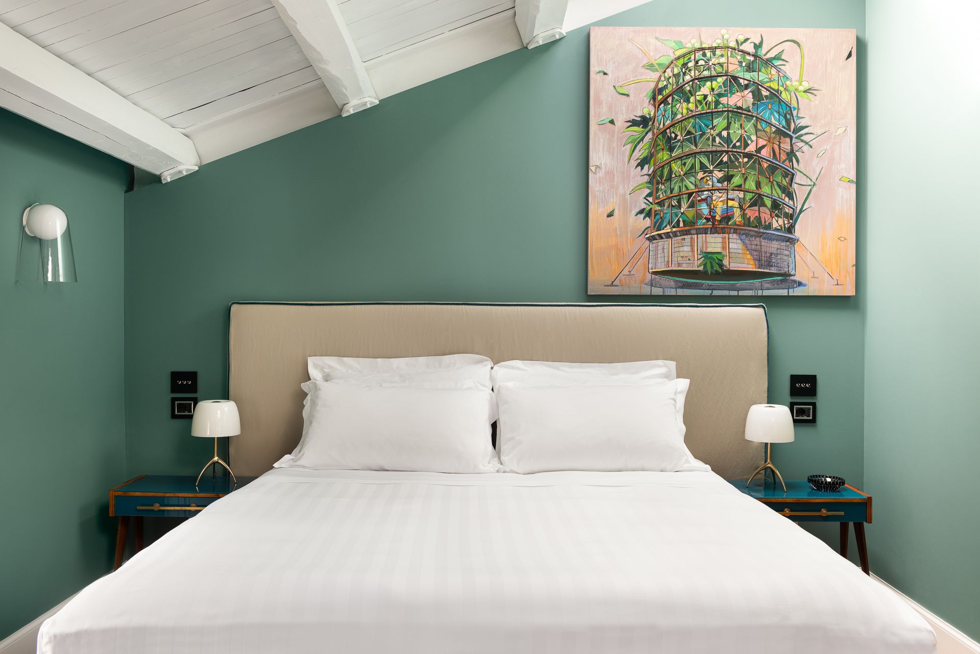 Bedroom with a bed, teal walls, artwork, and nightstands. White bedding, slanted ceiling.