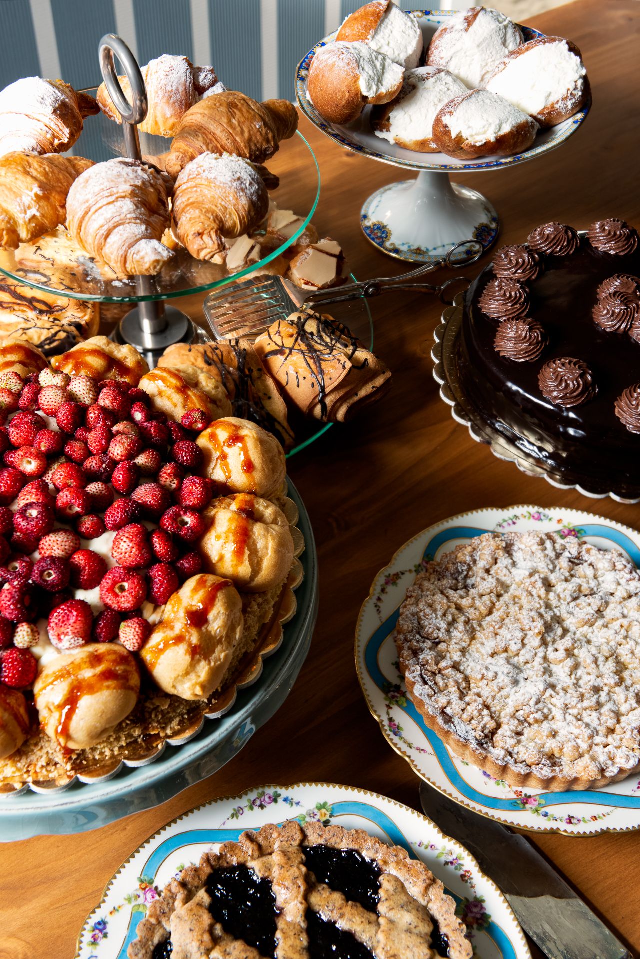 Assortment of pastries on a table: croissants, tarts with fruit, and a chocolate cake.