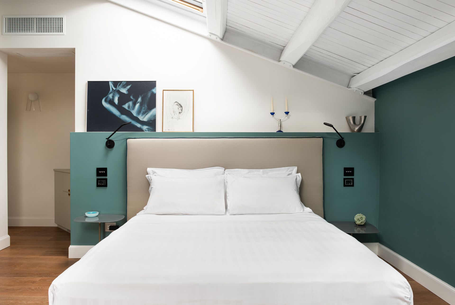 Bedroom with bed, teal accent wall, white ceiling, and artwork.