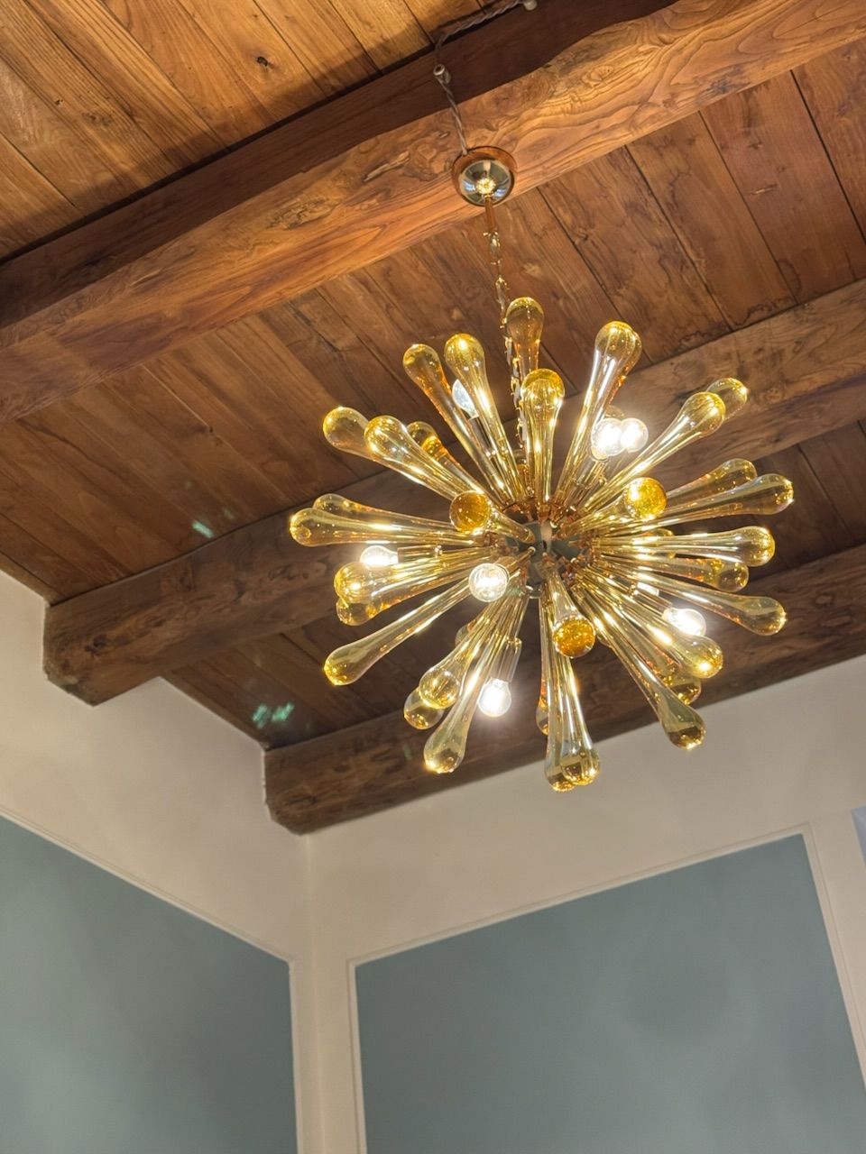 Gold starburst chandelier hanging from a wooden beam ceiling.