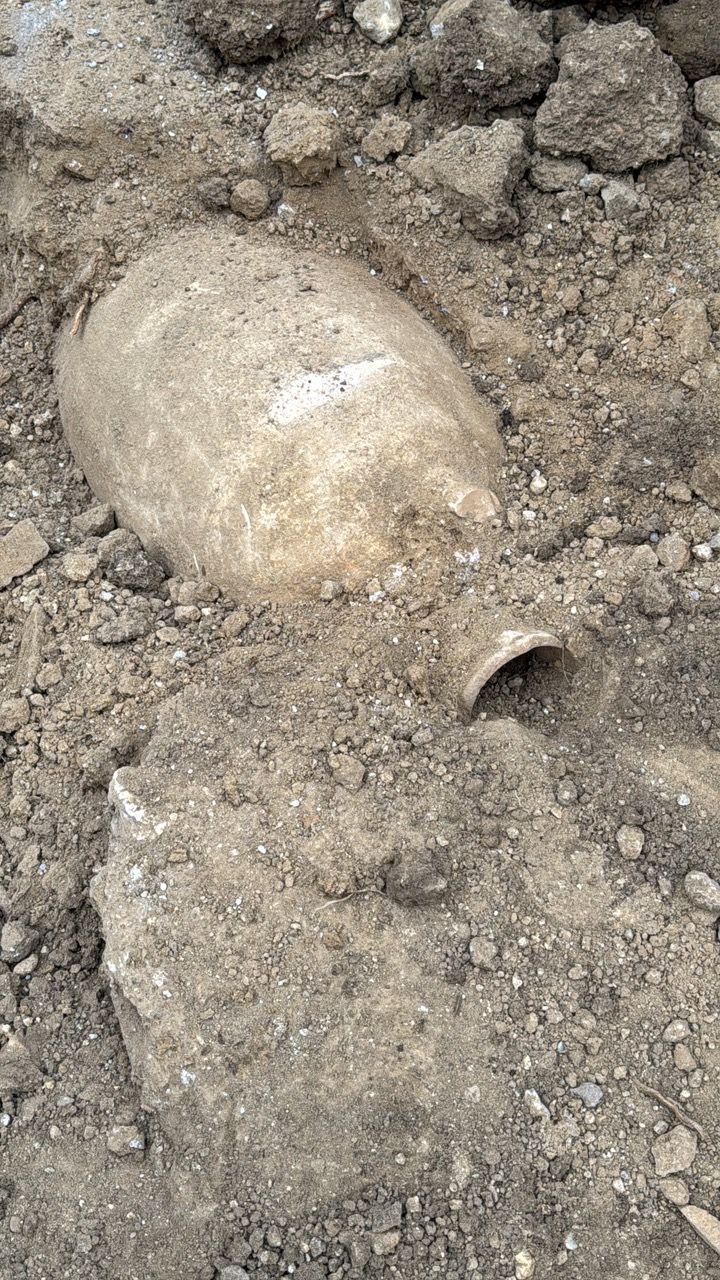 An antique, beige-colored amphora buried in dirt, partially uncovered.