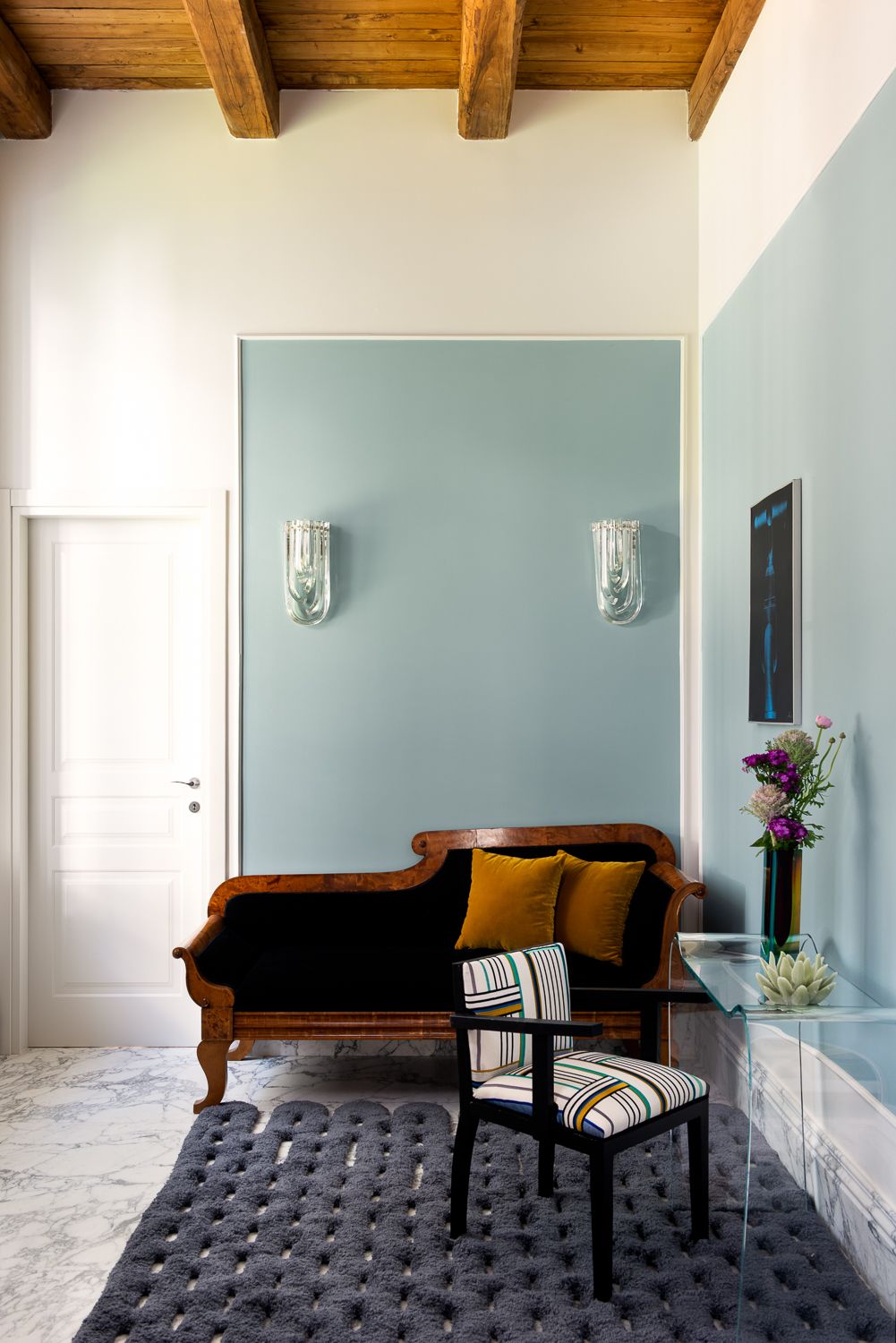 Interior with a dark wood chaise lounge, blue walls, a patterned chair, and a gray rug.