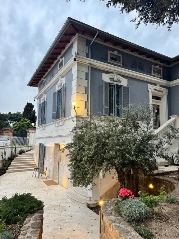 Edificio blu con finiture bianche, numerose finestre e tetto marrone. Un ulivo di fronte.