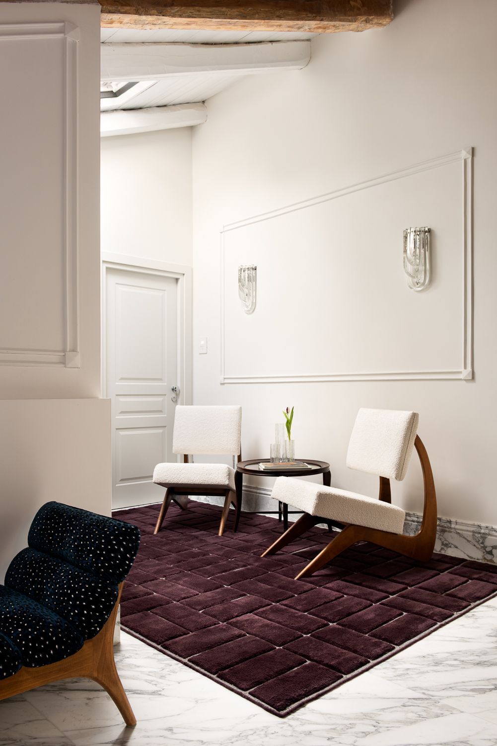 Un soggiorno moderno con sedie, un tappeto, un tavolino e una parete decorativa.
