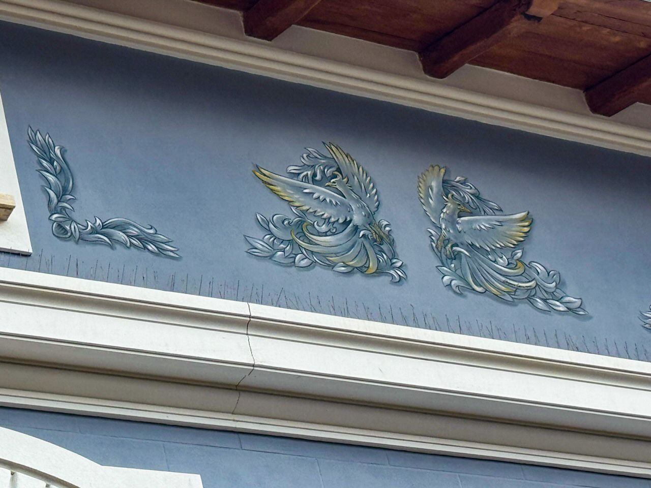 Facciata blu dell'edificio con ornamenti decorativi in ​​rilievo: foglie e due figure alate, accenti azzurri e dorati.