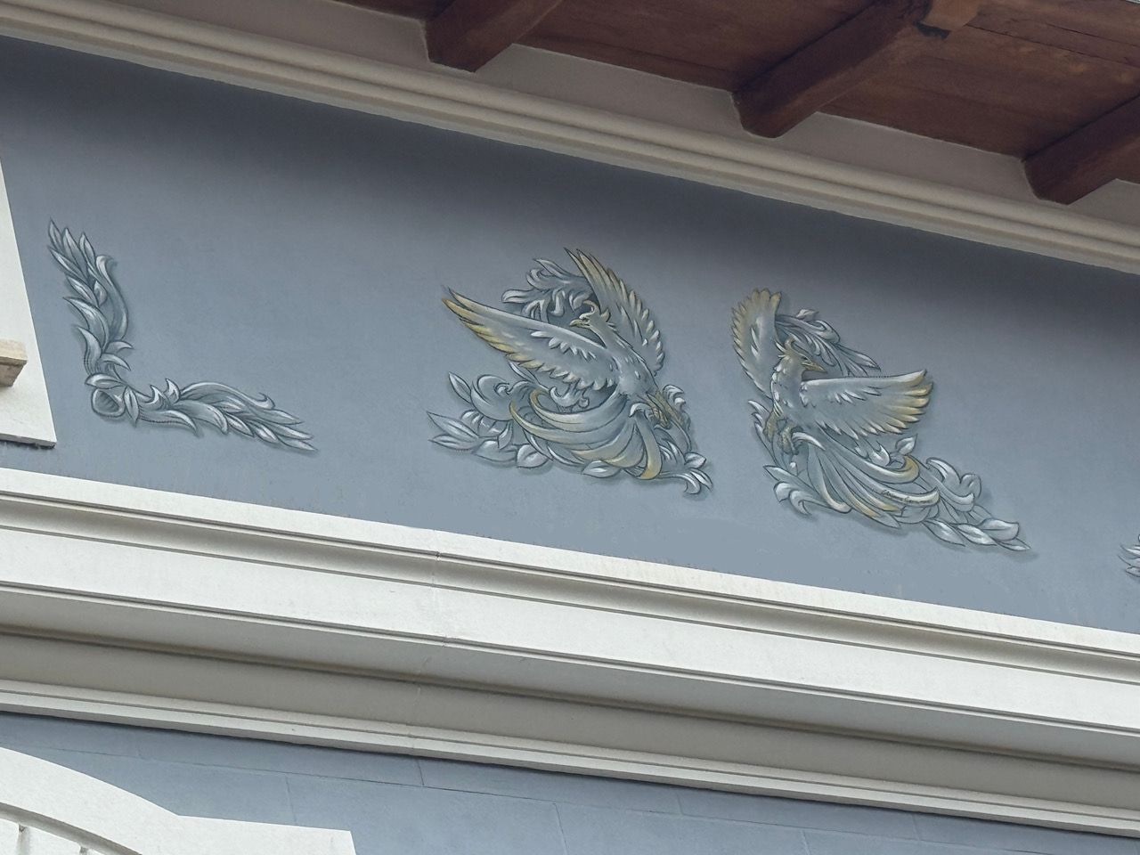 Blue building facade with decorative silver relief, including birds and leaves.