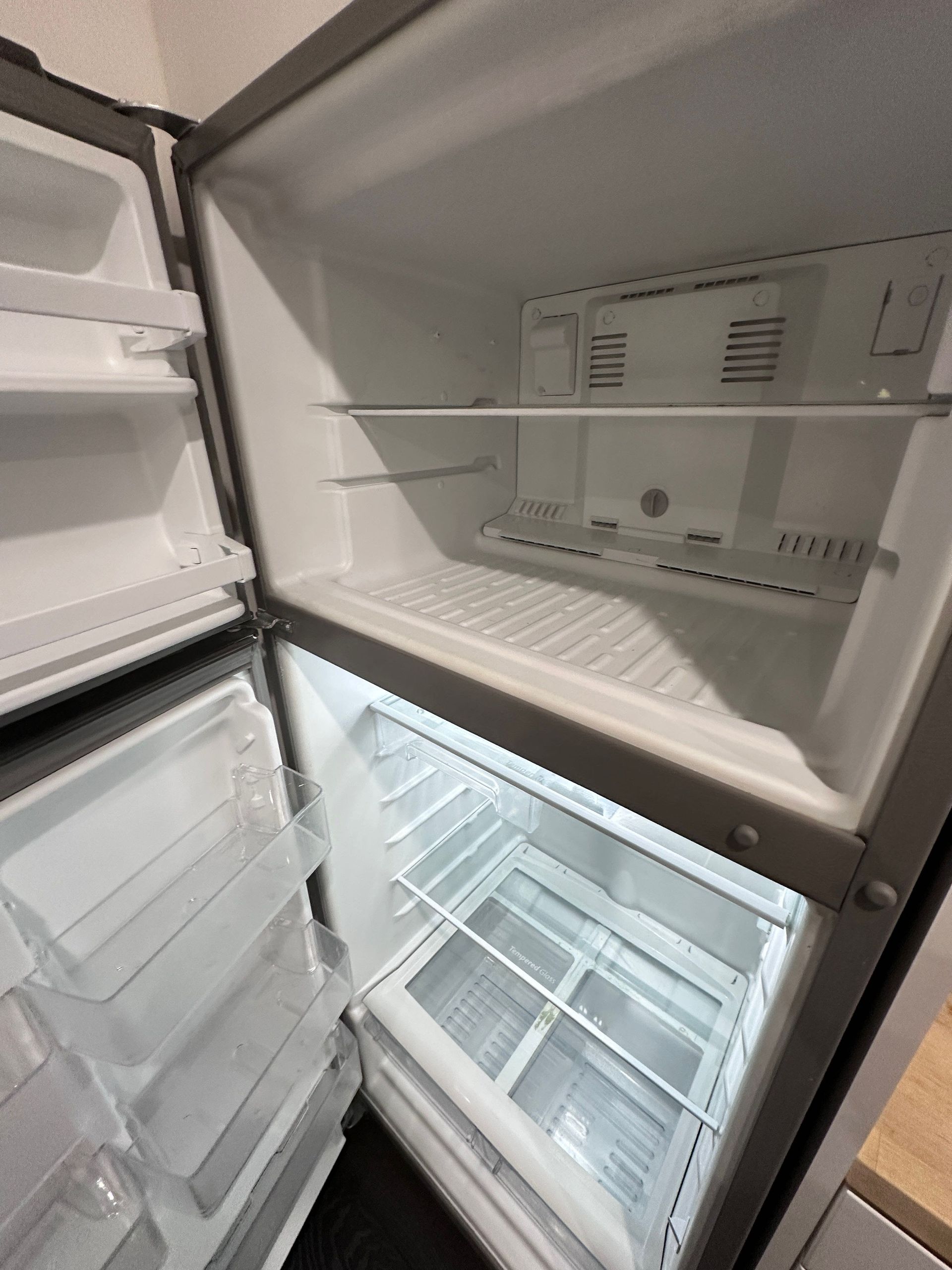 Open refrigerator with empty shelves, door bins, and a clear crisper drawer inside.