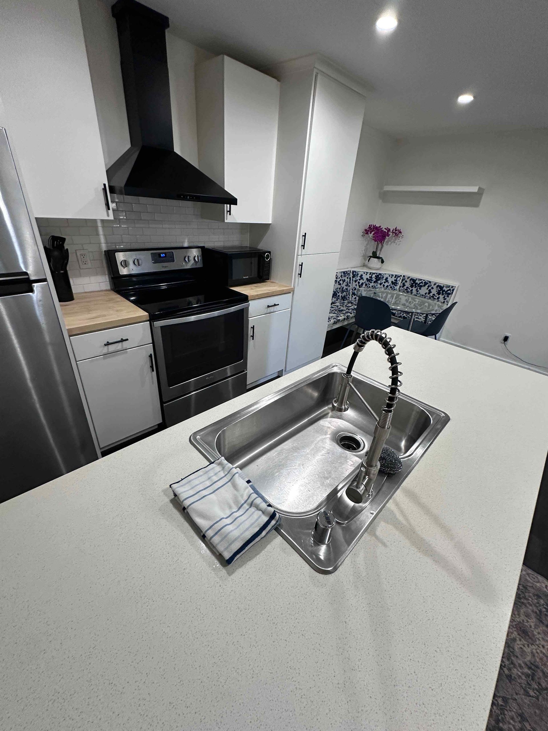 Modern kitchen with white cabinets, black stove, island sink, and gray countertops.