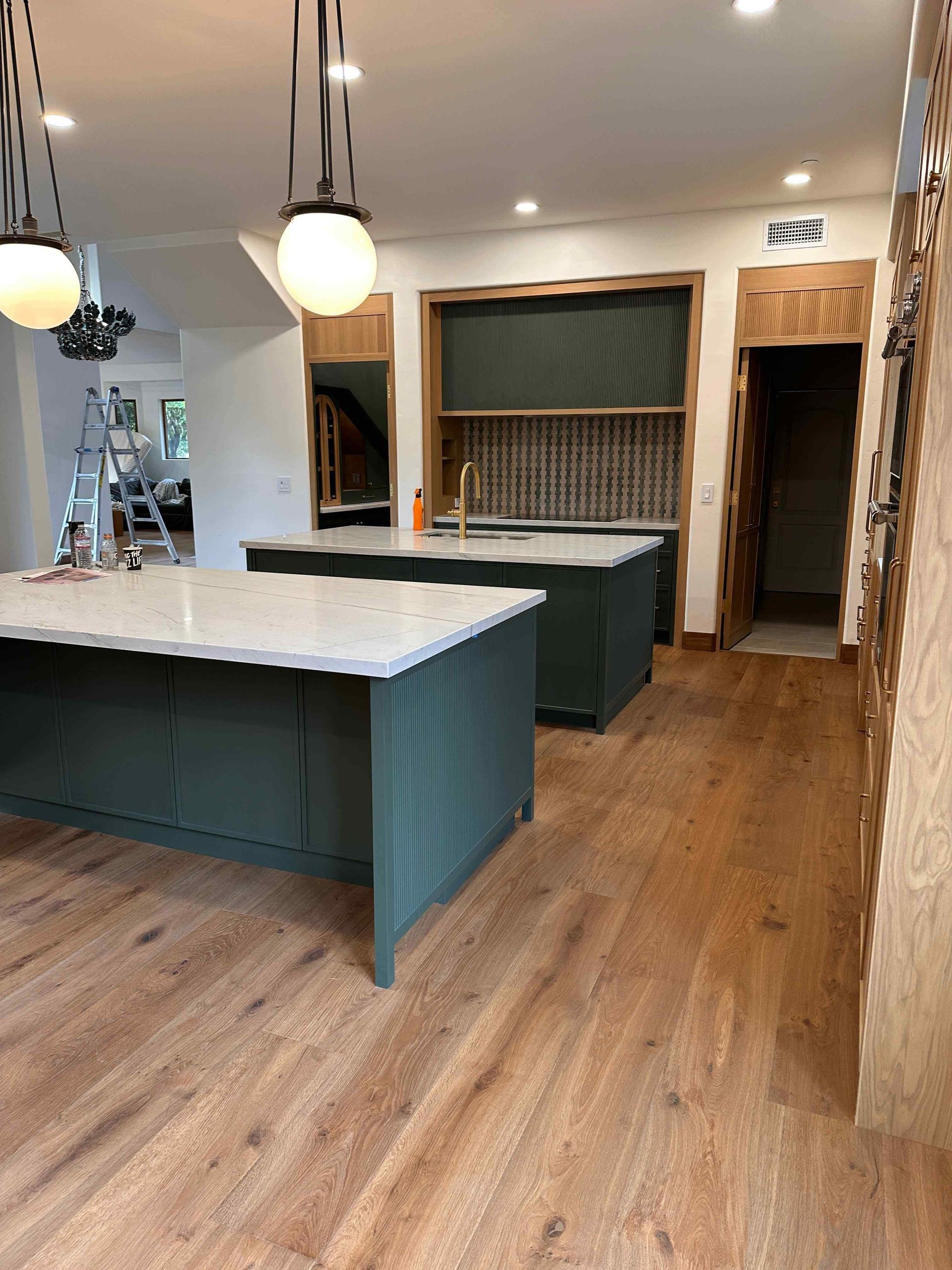 Modern kitchen with teal islands, wood floors, pendant lights, and built-in shelving.