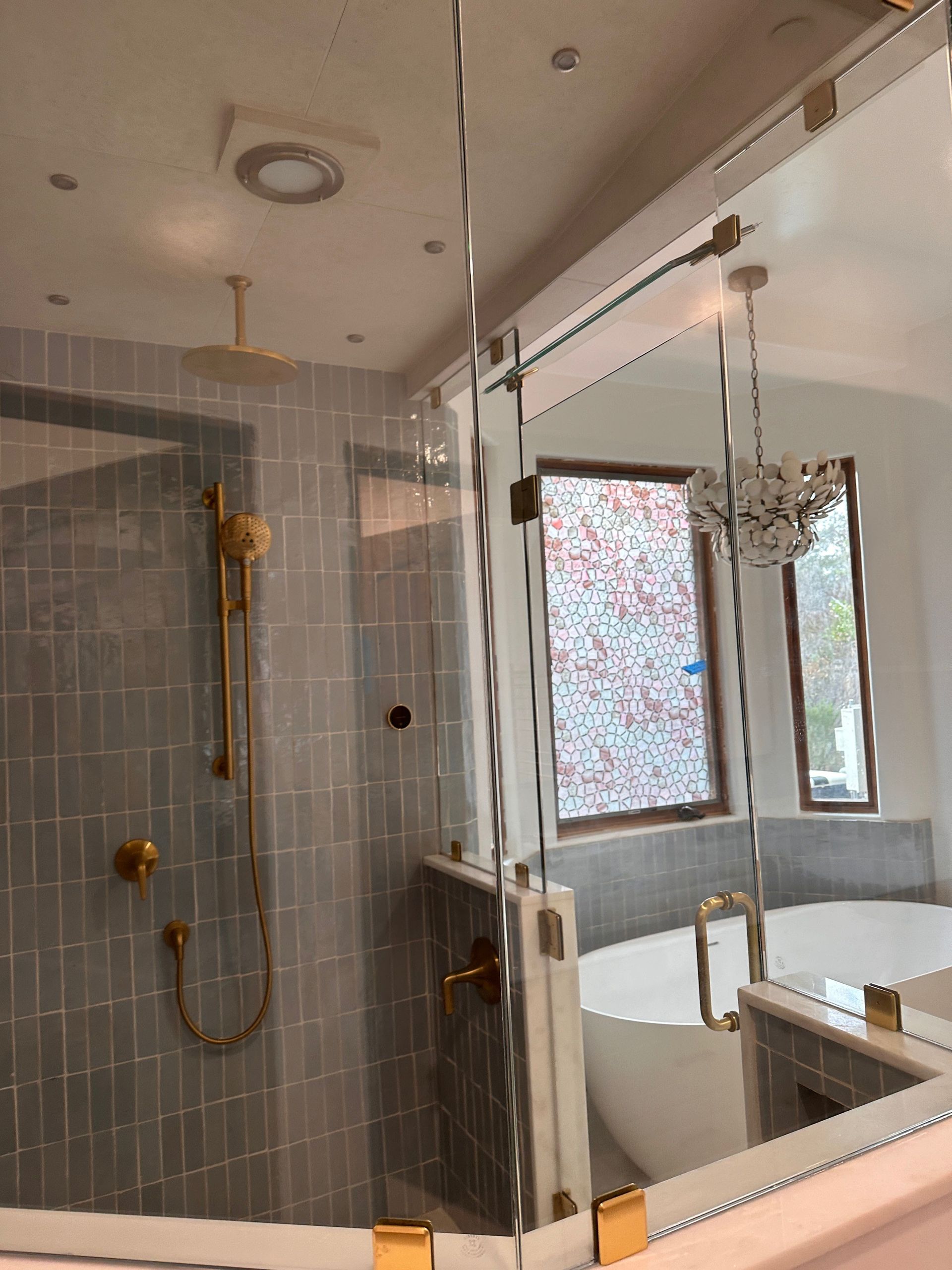 Modern bathroom with gray tiled shower, glass partition, and window beside a bathtub