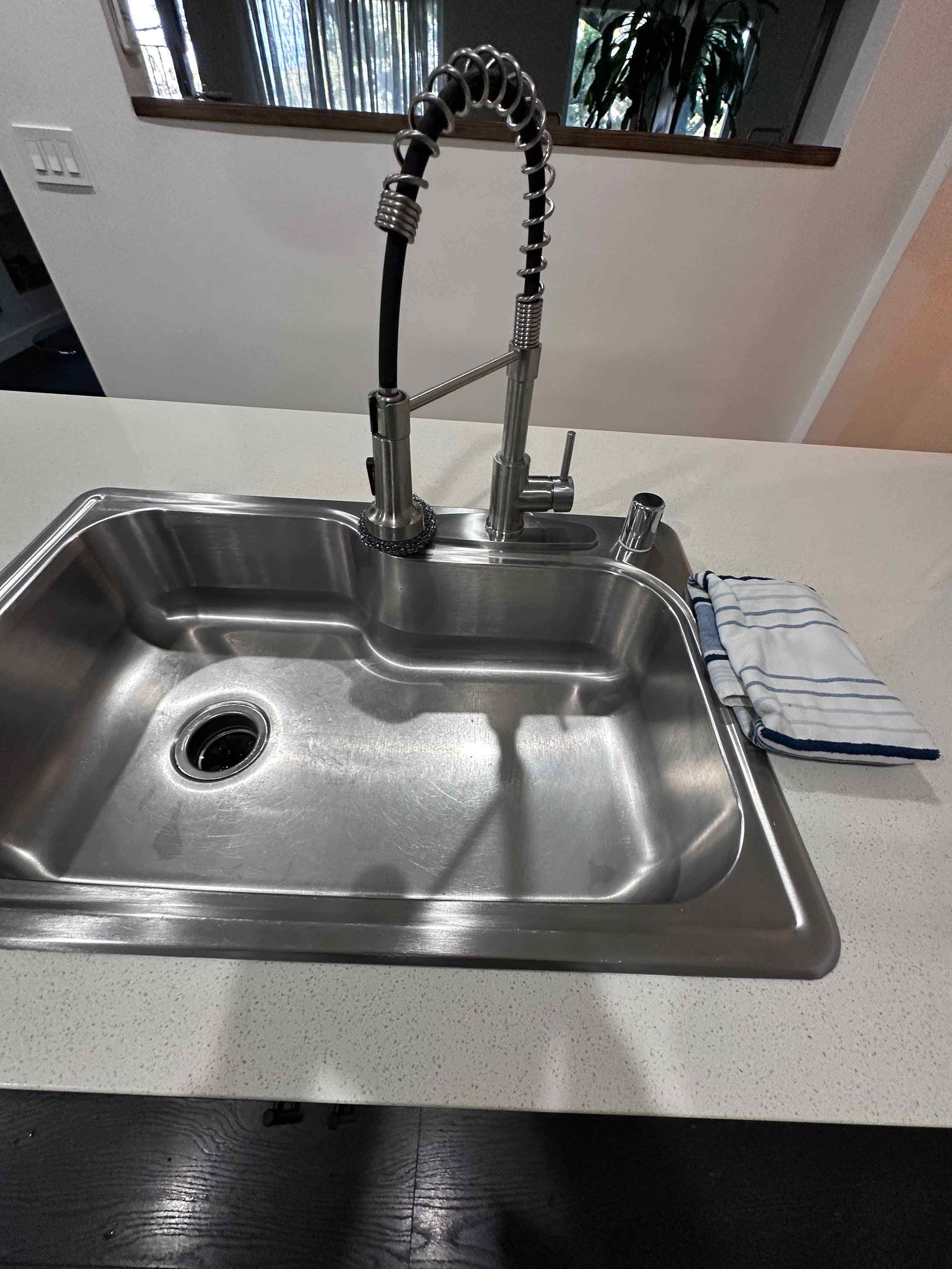 Kitchen sink with a high-arc faucet, countertop, and folded dish towel beside it.