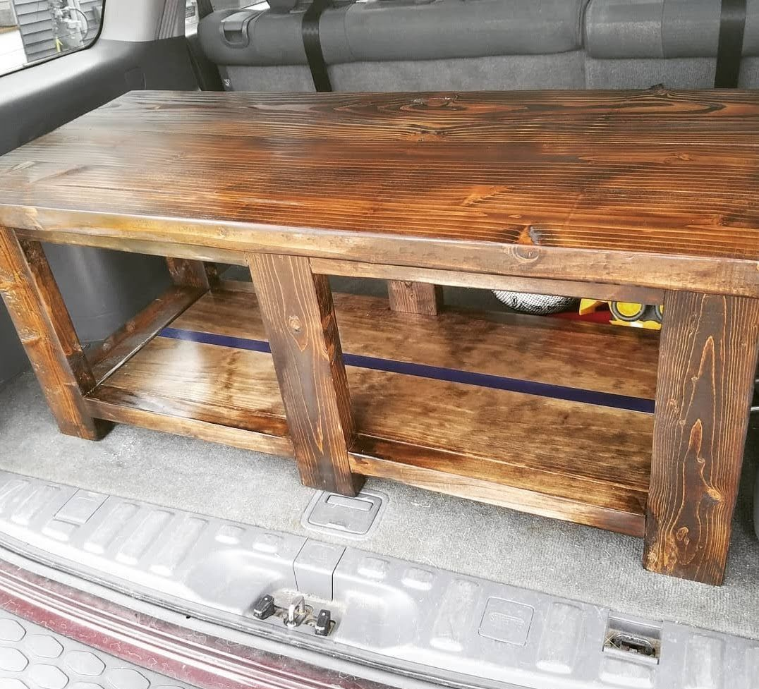 Wooden coffee table inside a vehicle trunk. Brown wood with a shelf, stained finish.