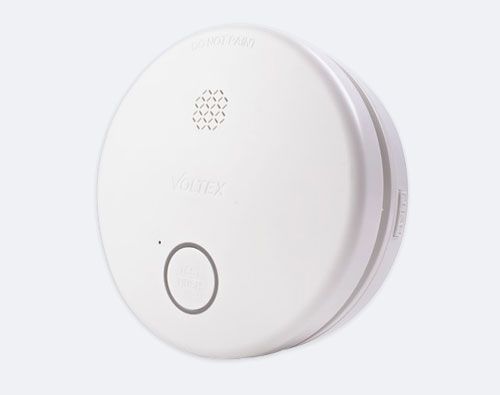 White Voltex smoke detector with a test/reset button mounted against a light background.