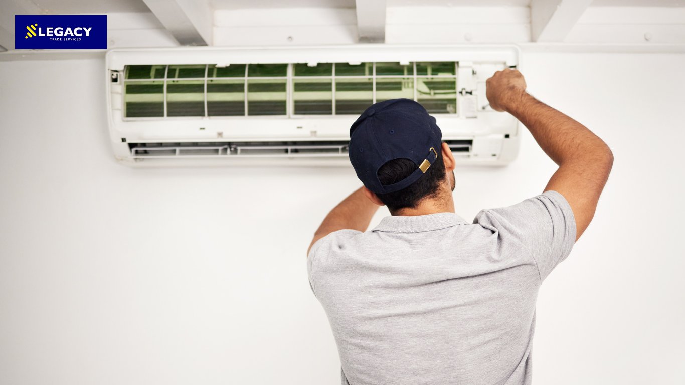 Technician servicing a wall-mounted air conditioner unit with the front cover open.