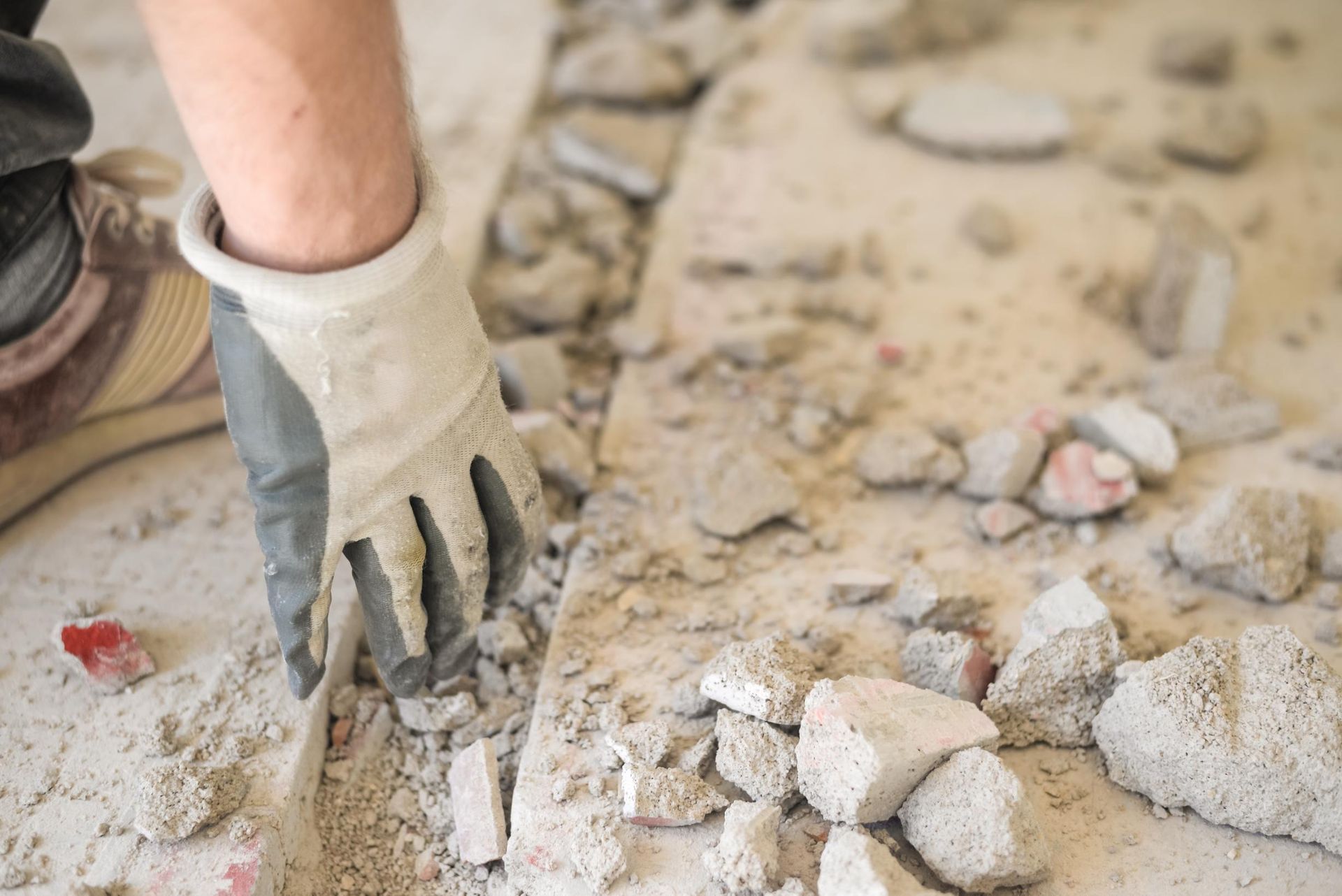 A gloved hand clears concrete debris from a trench in a floor during a construction or renovation project.