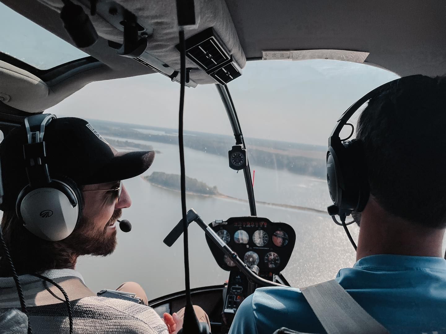 Two people in a helicopter cockpit, one is piloting. View of a river through the windshield.