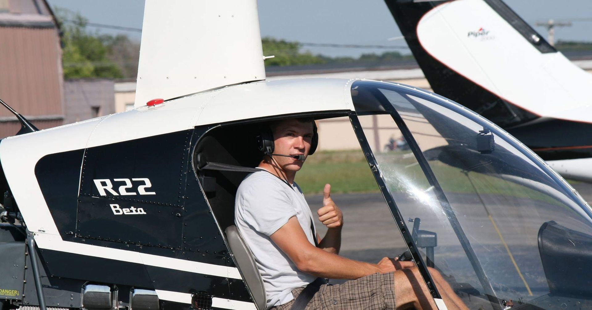 Man in R22 Beta helicopter cockpit gives thumbs up.