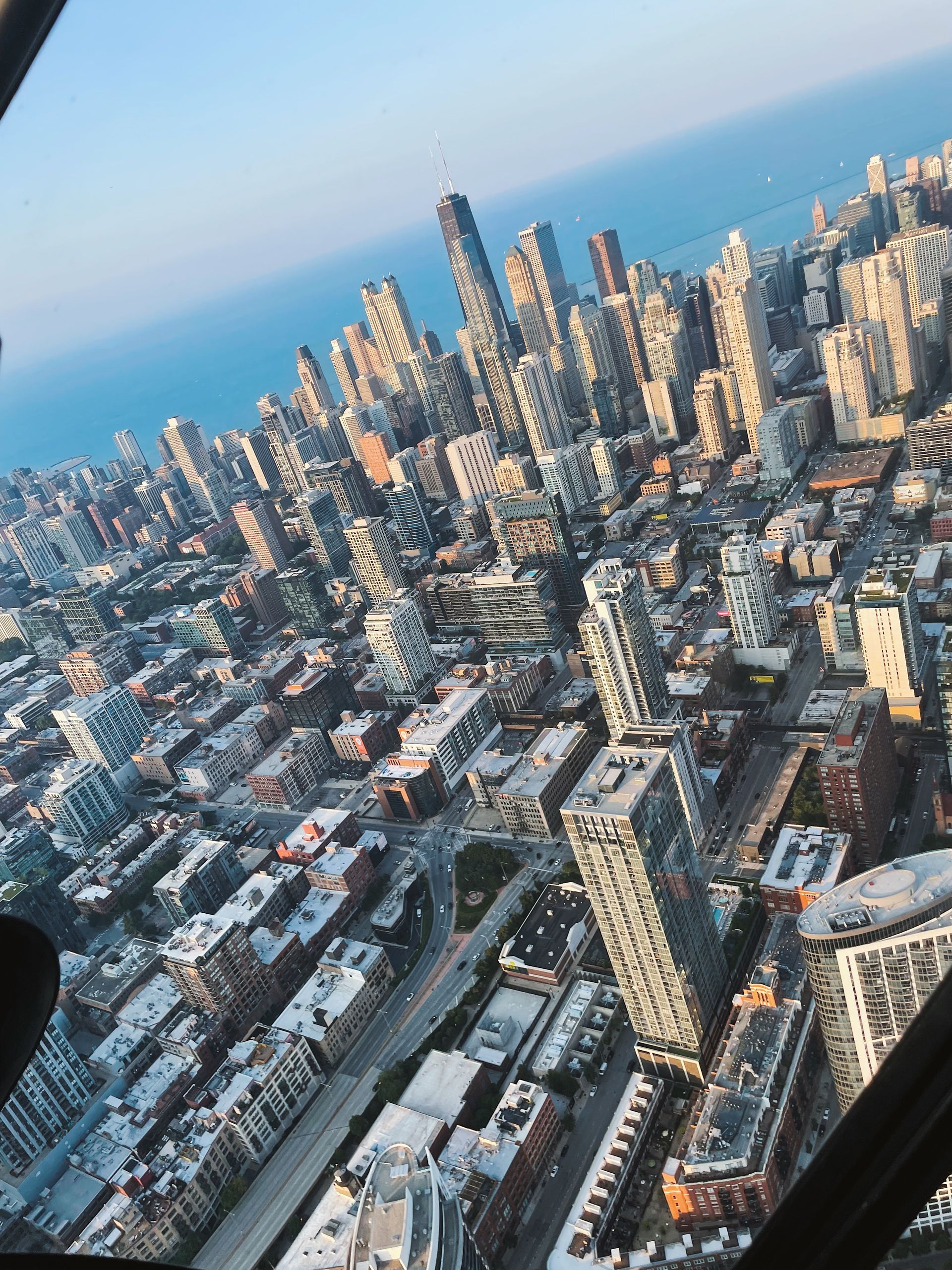 Aerial view of a dense city with tall buildings near a body of water under a clear sky.