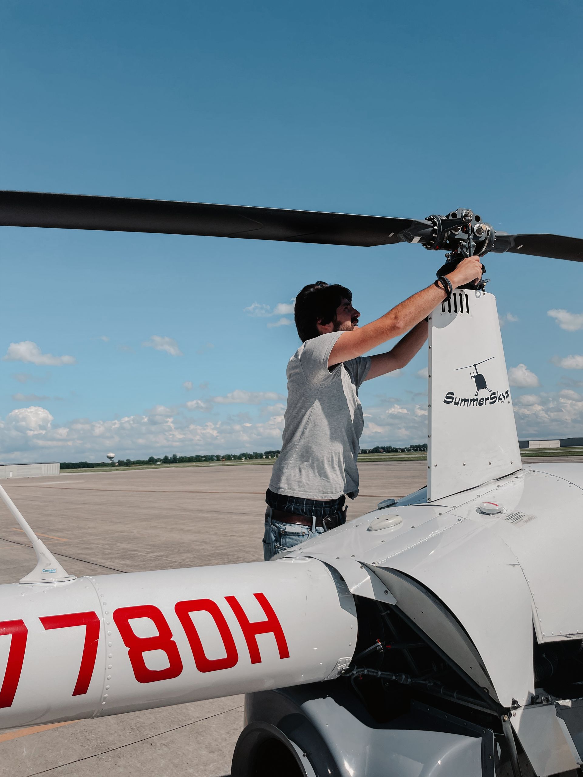 Person working on the rotor blades of a white helicopter, in an airport on a sunny day.