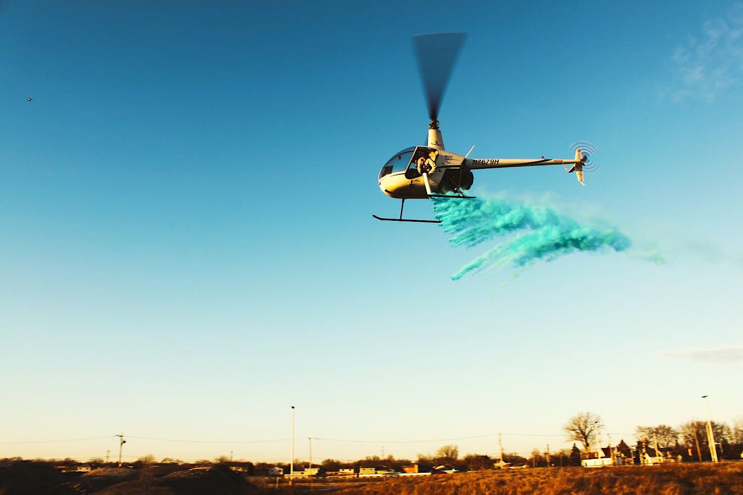 Helicopter releasing blue powder into the air during a gender reveal; blue sky, rural setting.