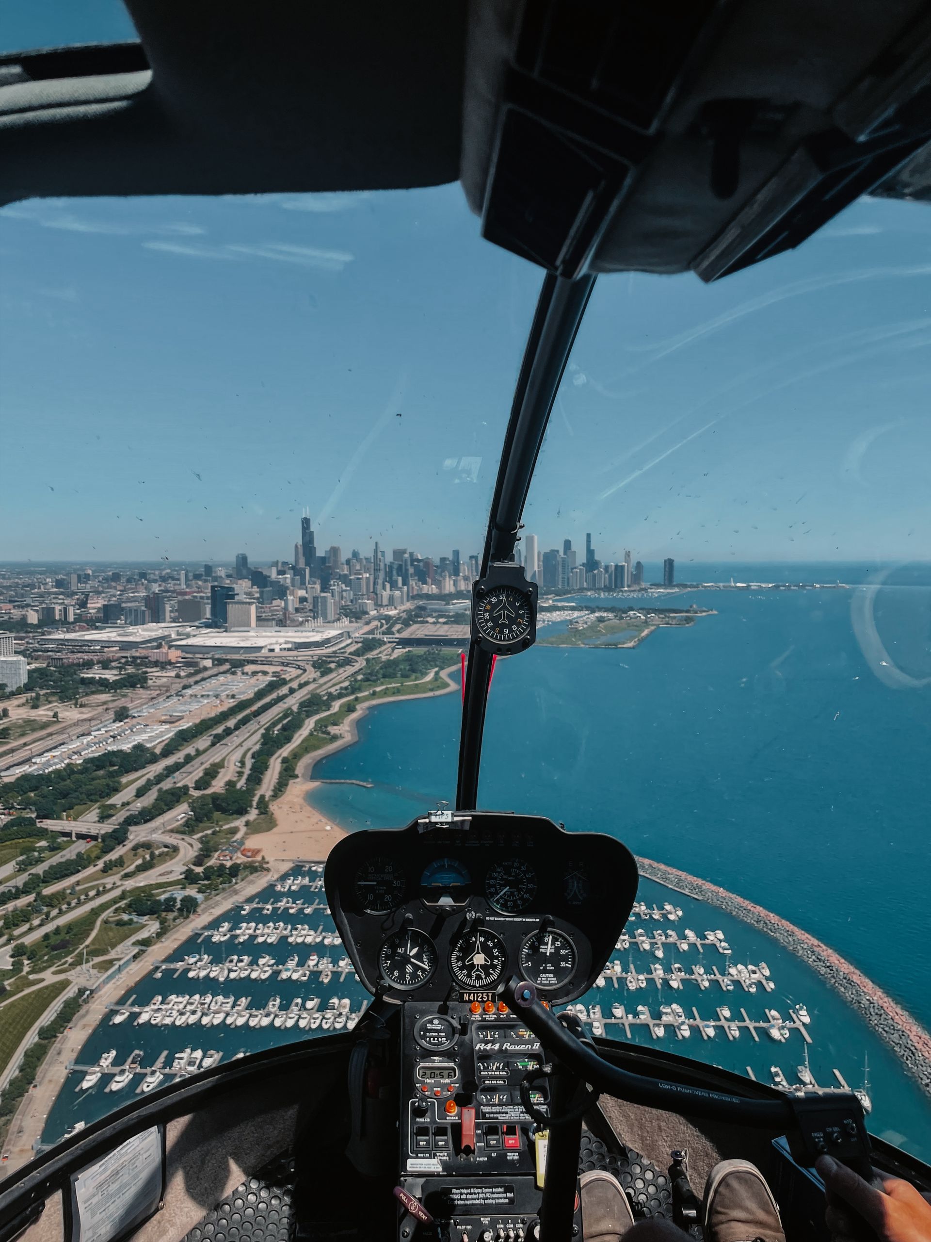 Helicopter cockpit view of Chicago skyline, blue water, and boats on a sunny day.