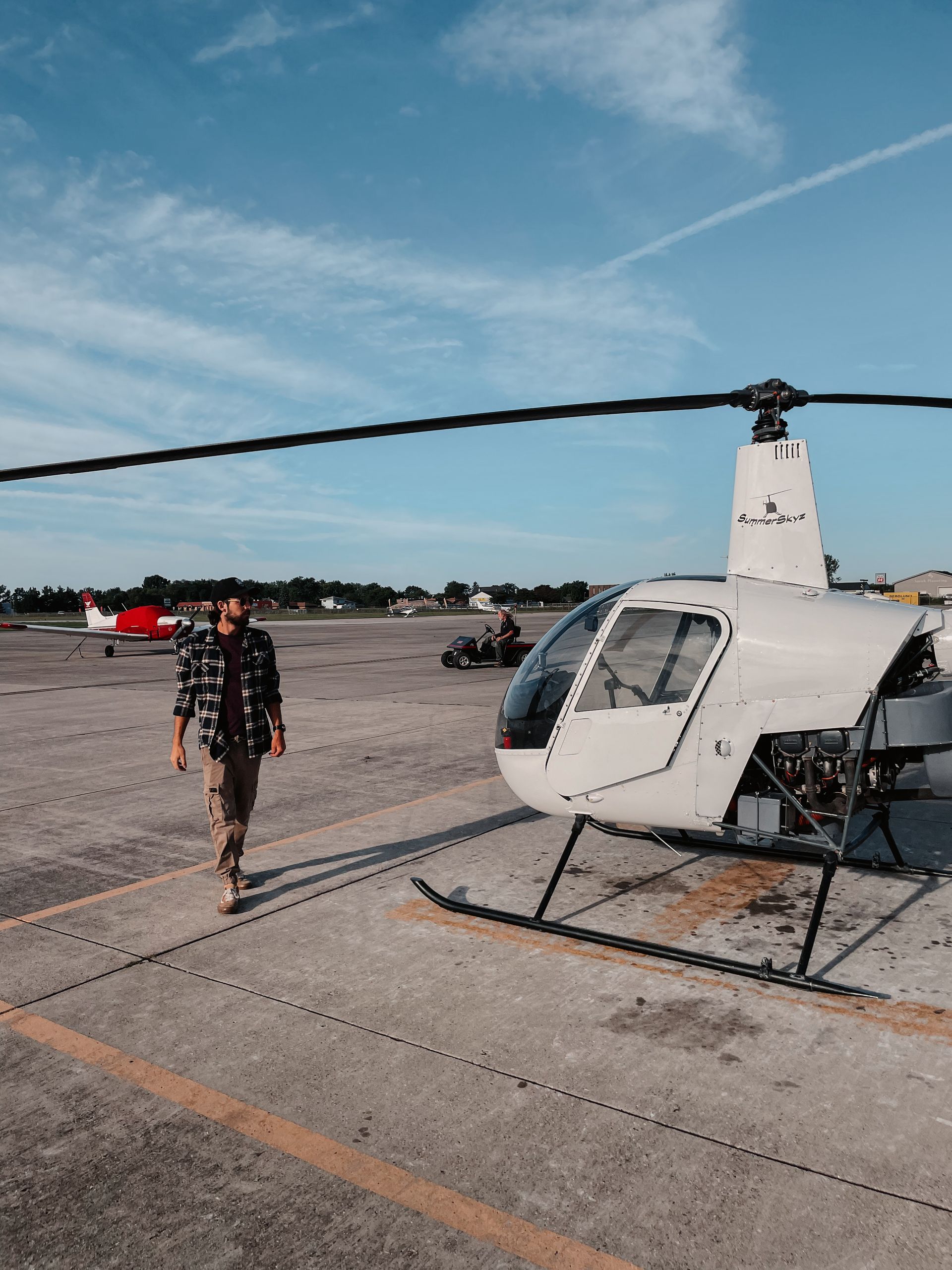Man walks towards a white helicopter on a concrete airfield, blue sky overhead.