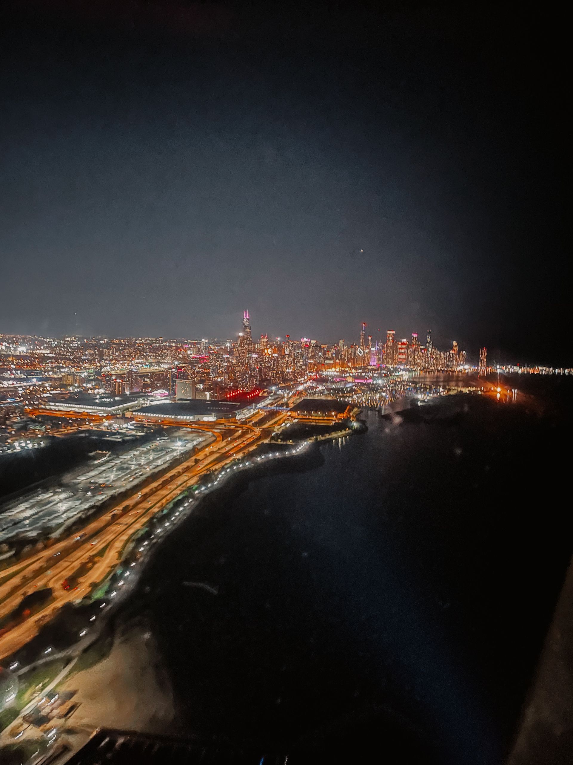 Night view of a city skyline, with bright lights along the coast, over a dark sea.