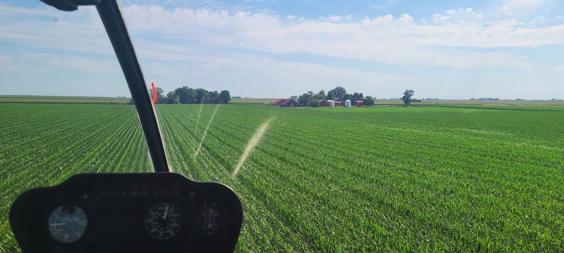 A helicopter view of green crops being watered, blue sky above.