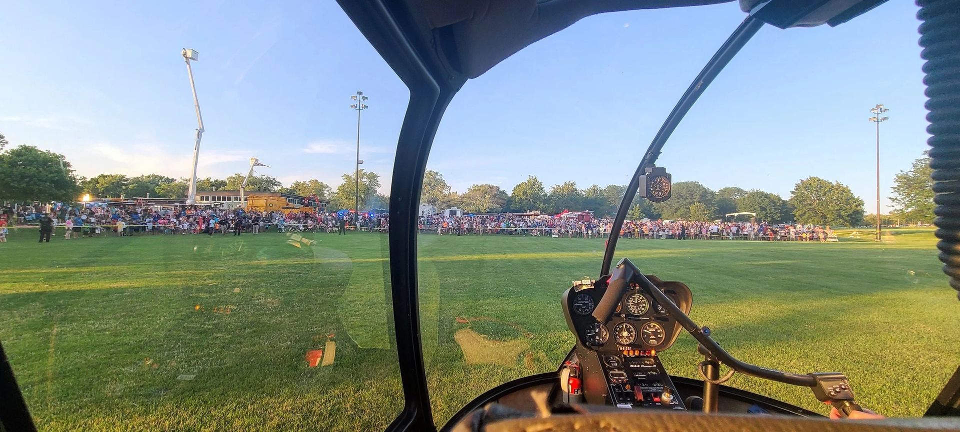 View from inside a helicopter of a large crowd in a grassy field on a sunny day.