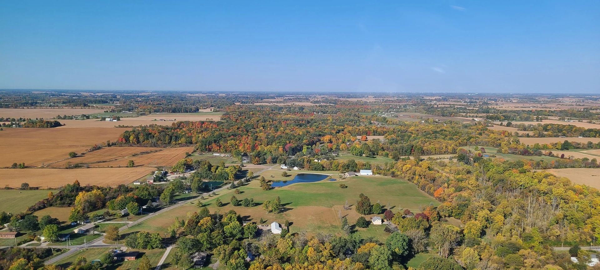 Aerial view of farmland and forest under a clear blue sky.
