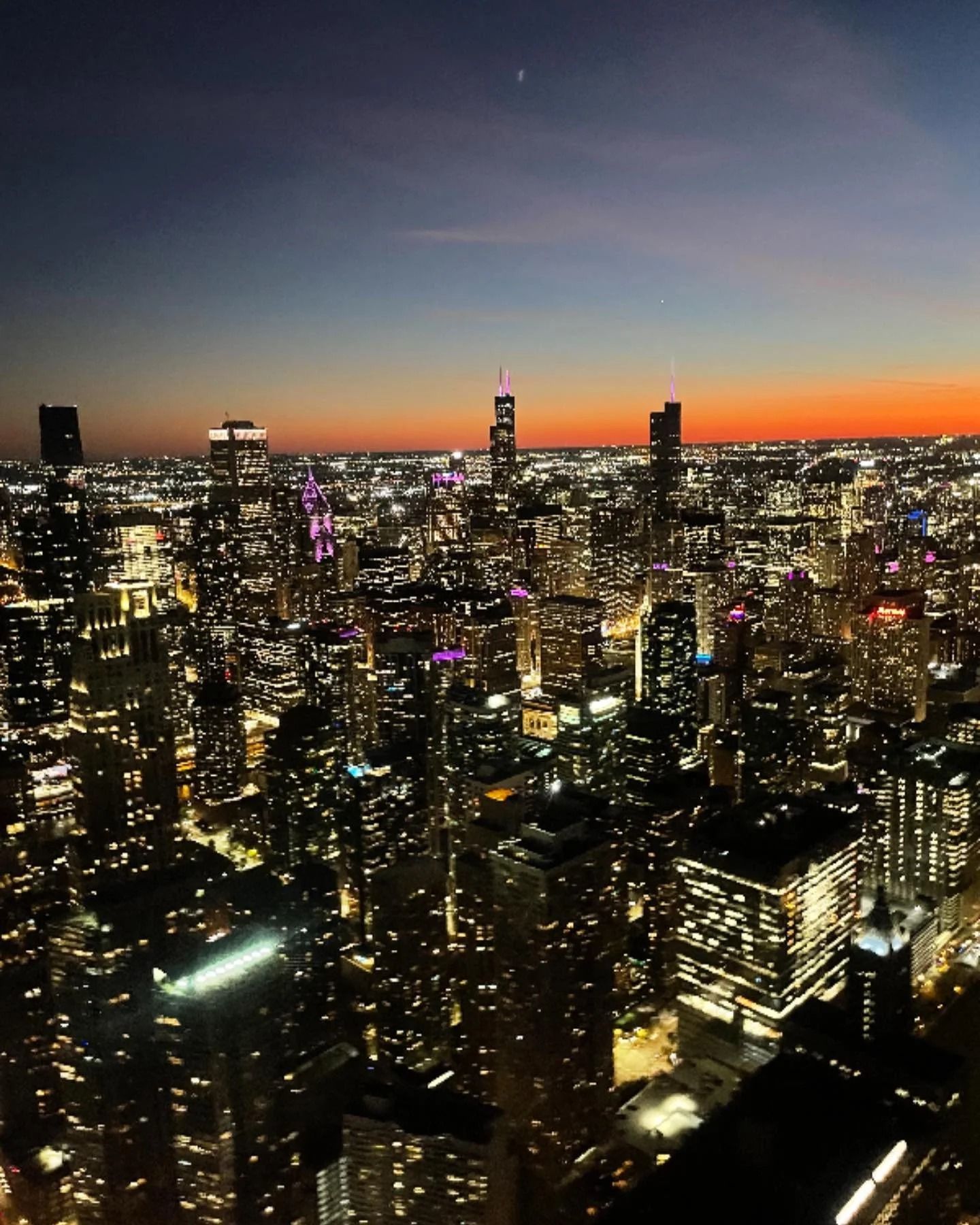 Night view of a cityscape at dusk, featuring lit skyscrapers and a colorful sky.