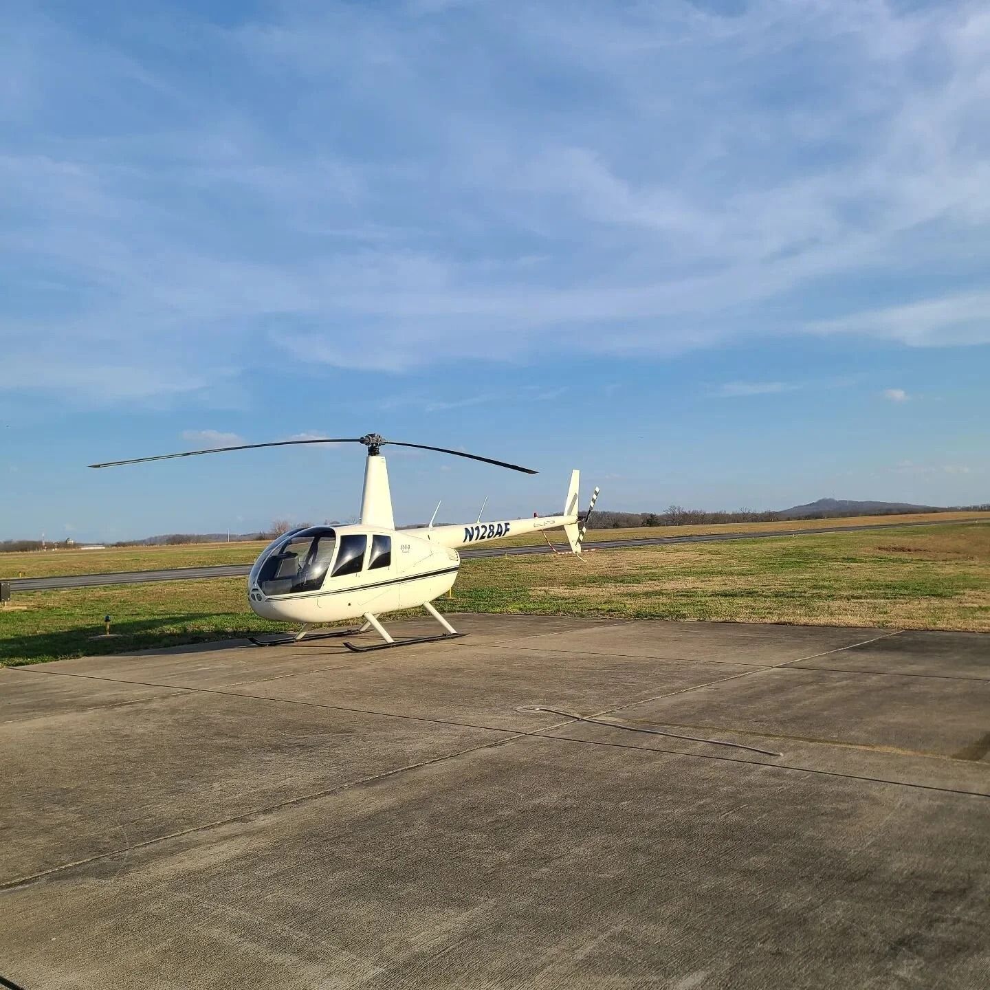 White helicopter on concrete landing pad with blue sky in the background.
