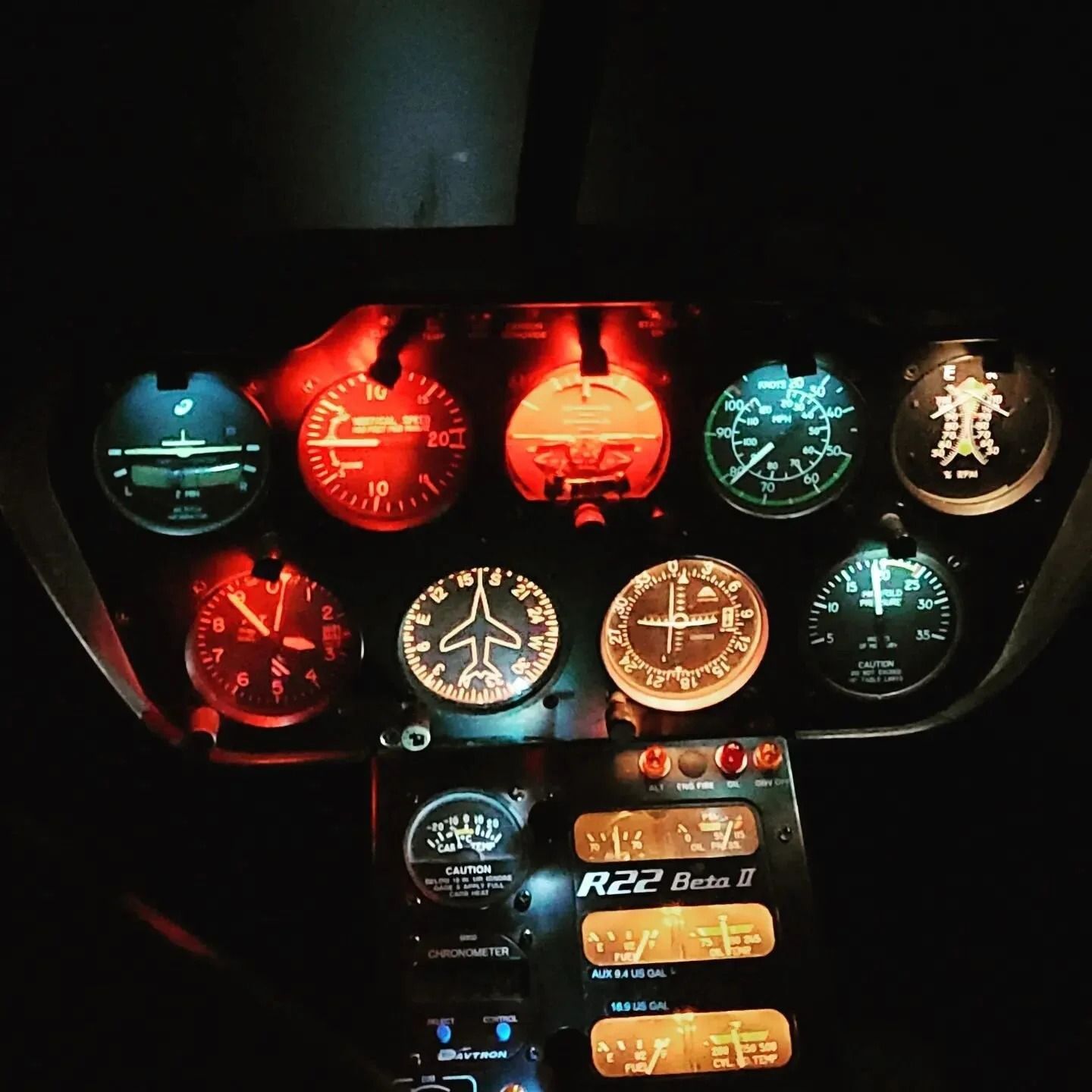Helicopter cockpit, illuminated gauges. Red and blue instrument lights glow against dark interior.