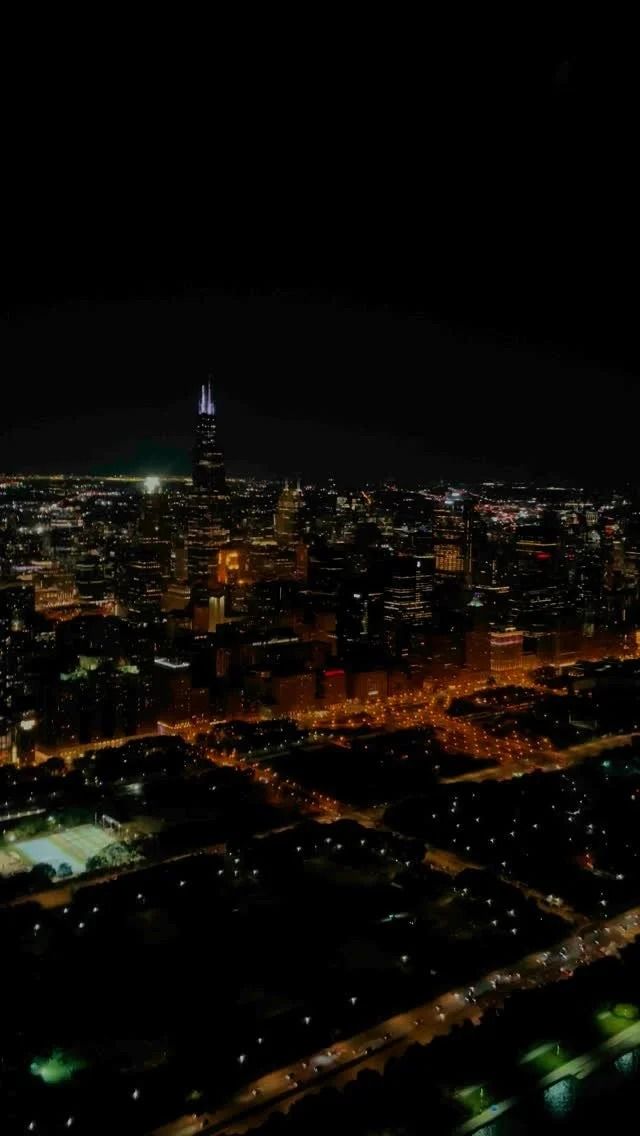Nighttime aerial view of Chicago skyline, with illuminated buildings and dark sky.