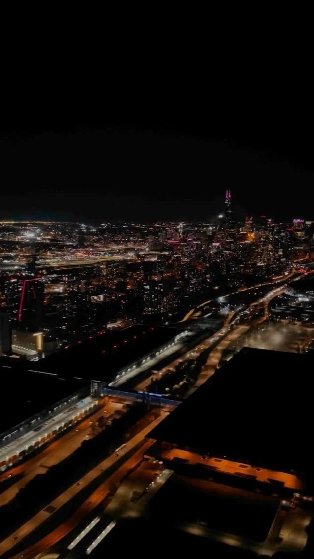Nighttime cityscape with illuminated buildings and a highway.
