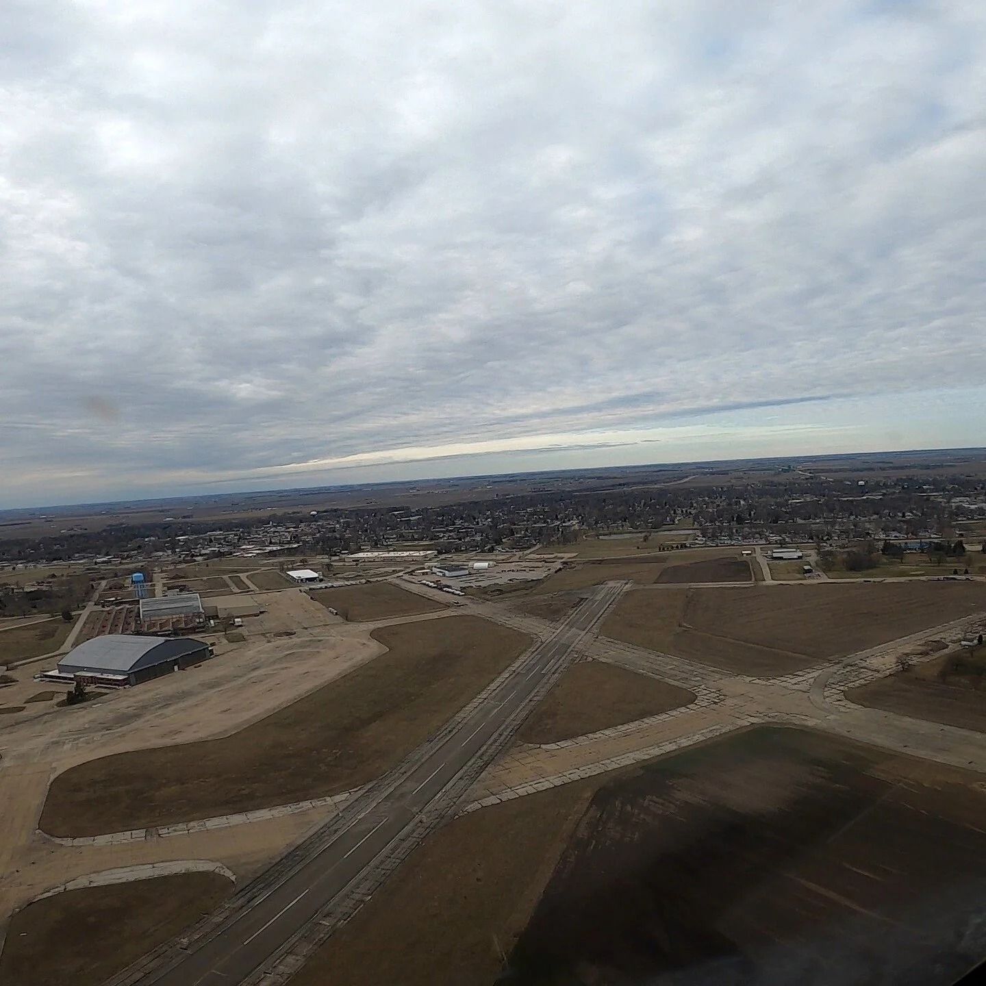 Aerial view of an airfield with runways, a town in the distance, and a cloudy sky.