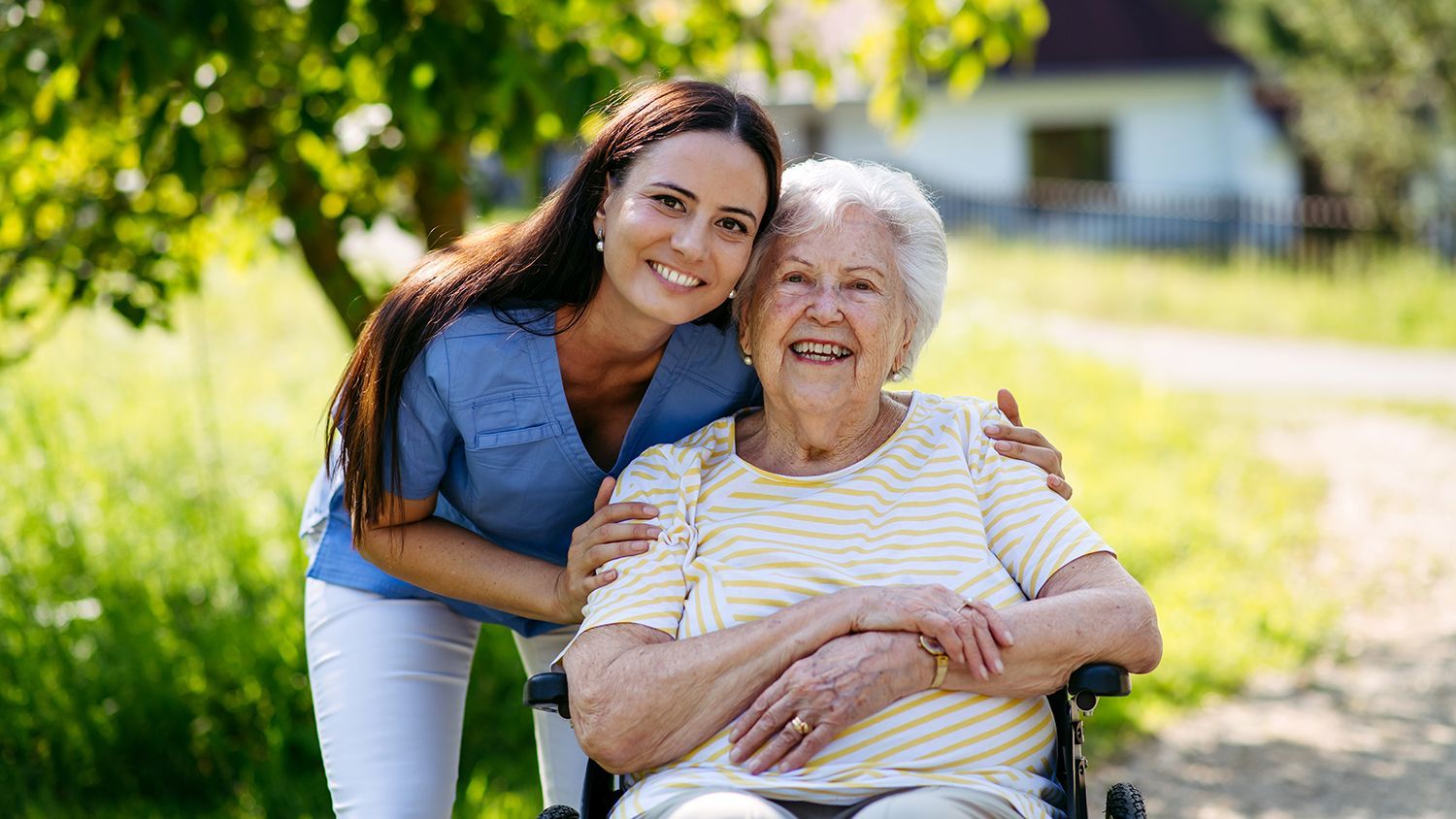 In-home care caregiver assisting a smiling senior in a wheelchair outdoors.
