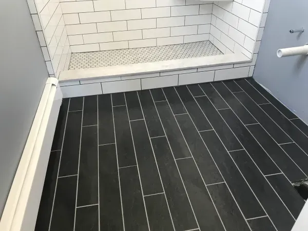 Black tiled bathroom floor with white-tiled shower stall and gray walls.